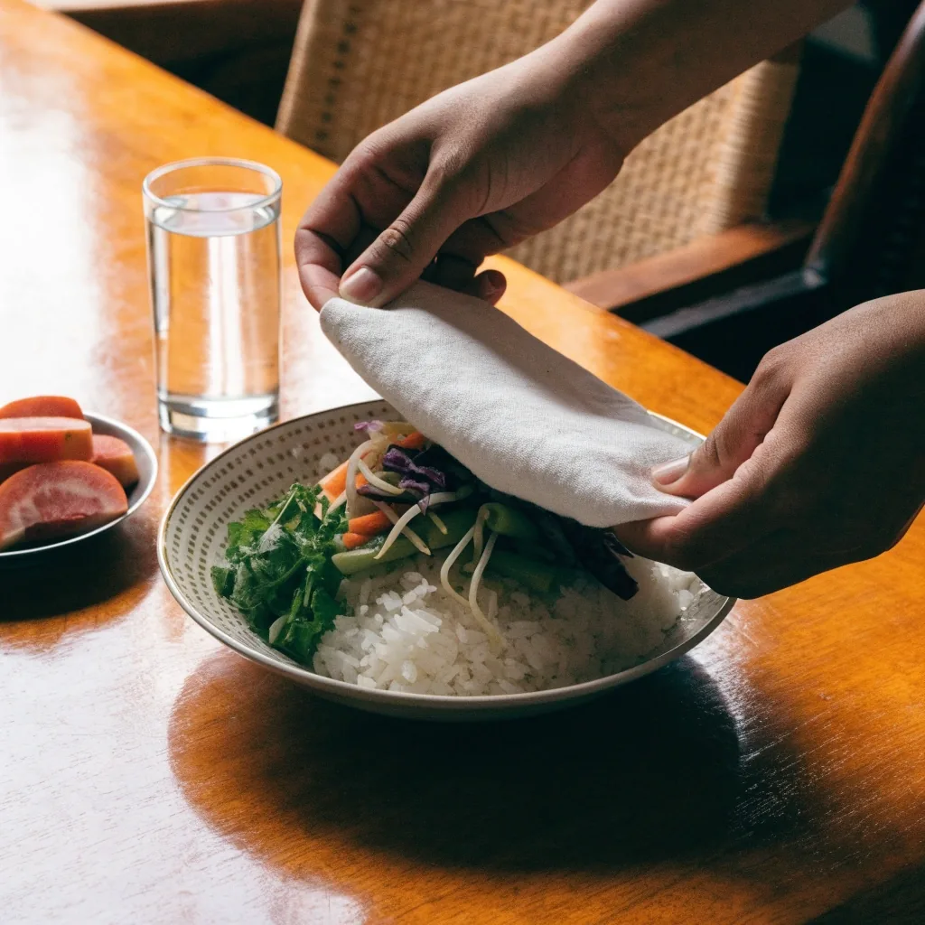 A covered plate, glass of water and fresh produce arranged on an Indonesian dining table